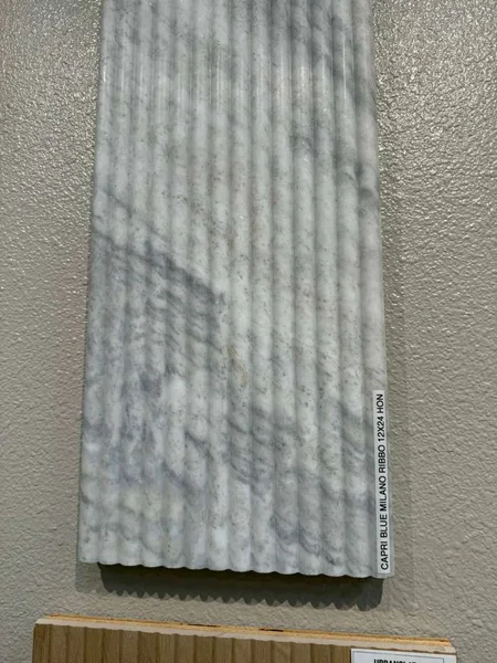 A pale fluted surface with repeating ridges and soft shadows.